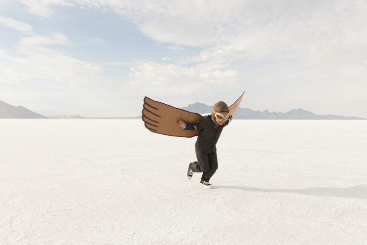 A young business boy dressed in business suit wearing cardboard wings and aviator goggles is ready to fly his business into the sky. He is running on the Bonneville Salt Flats in Utah, USA.