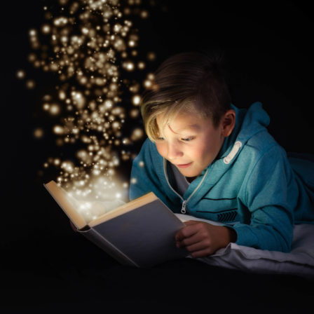 blond boy reading a magicical story book with light leaping off the page